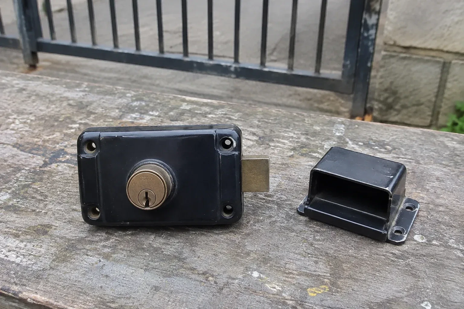 Detached rim gate lock and separate box keeper on an outdoor workbench. — Gate & Building Entry Locks, Toronto